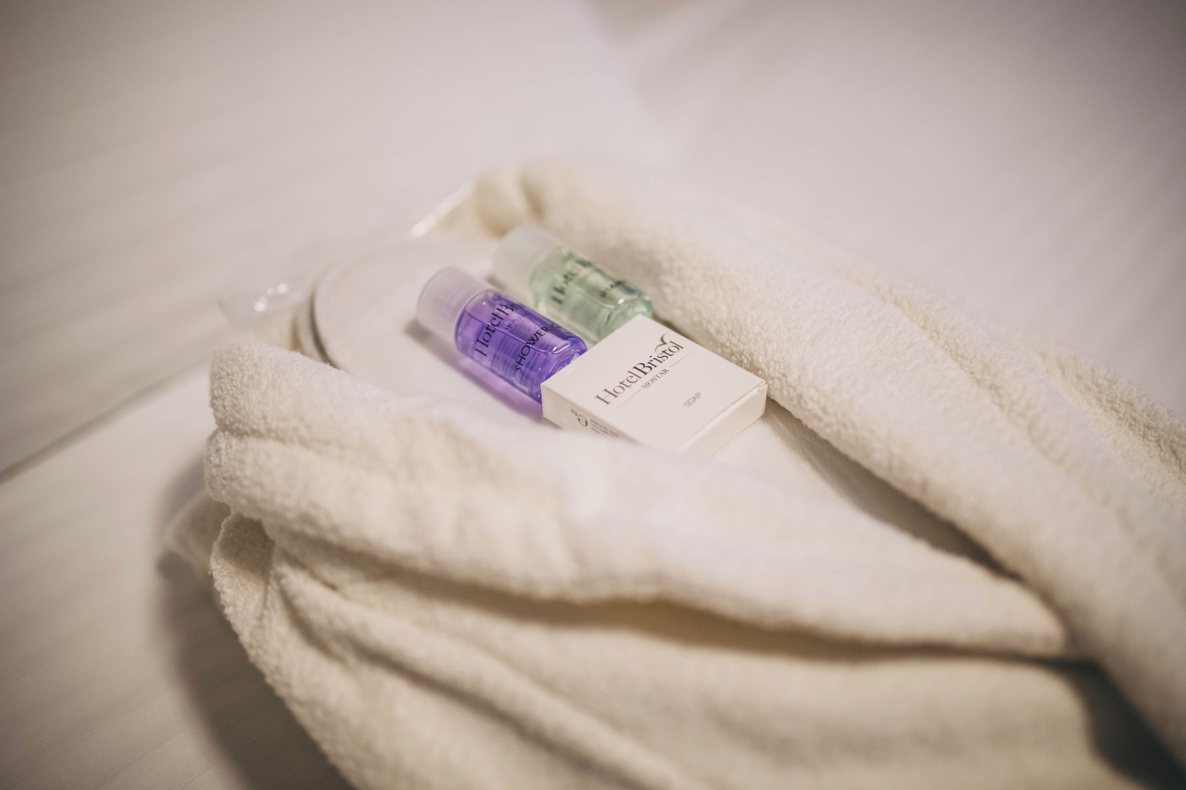 A white towel with a bottle of lotion and a small box, possibly a toiletry item, on a bed.