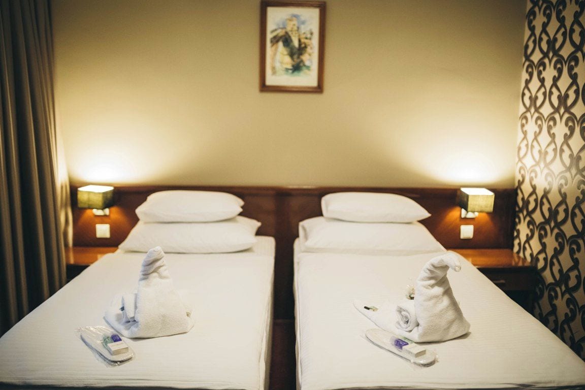 Two twin beds with white linens, each with a rolled towel and a remote control.