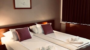 Quarto de hotel com duas camas, um quadro na parede, aparelho de ar condicionado e uma janela com cortinas.
