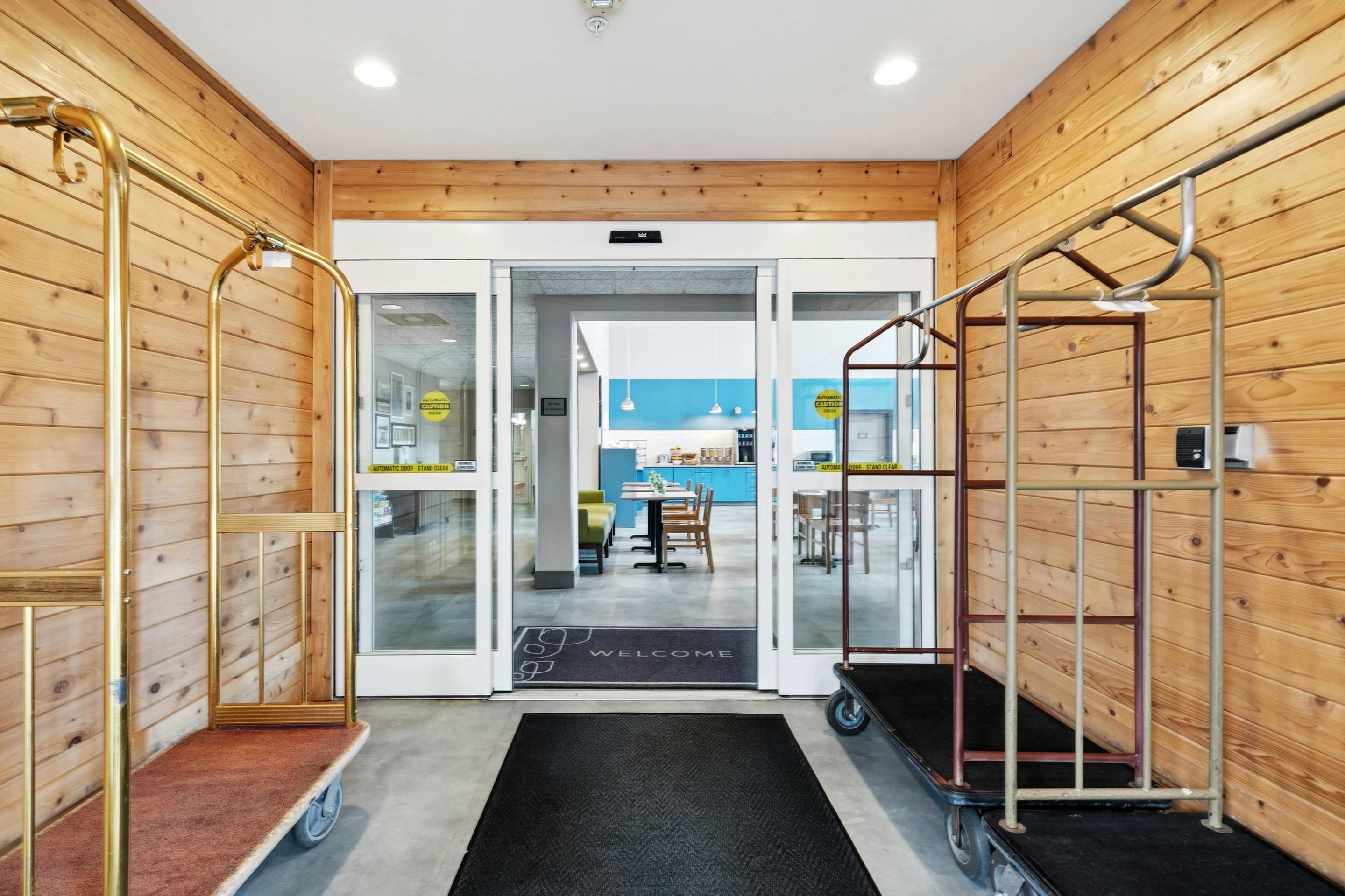 A hotel lobby with wooden walls, a reception desk, and a dining area visible through glass doors.