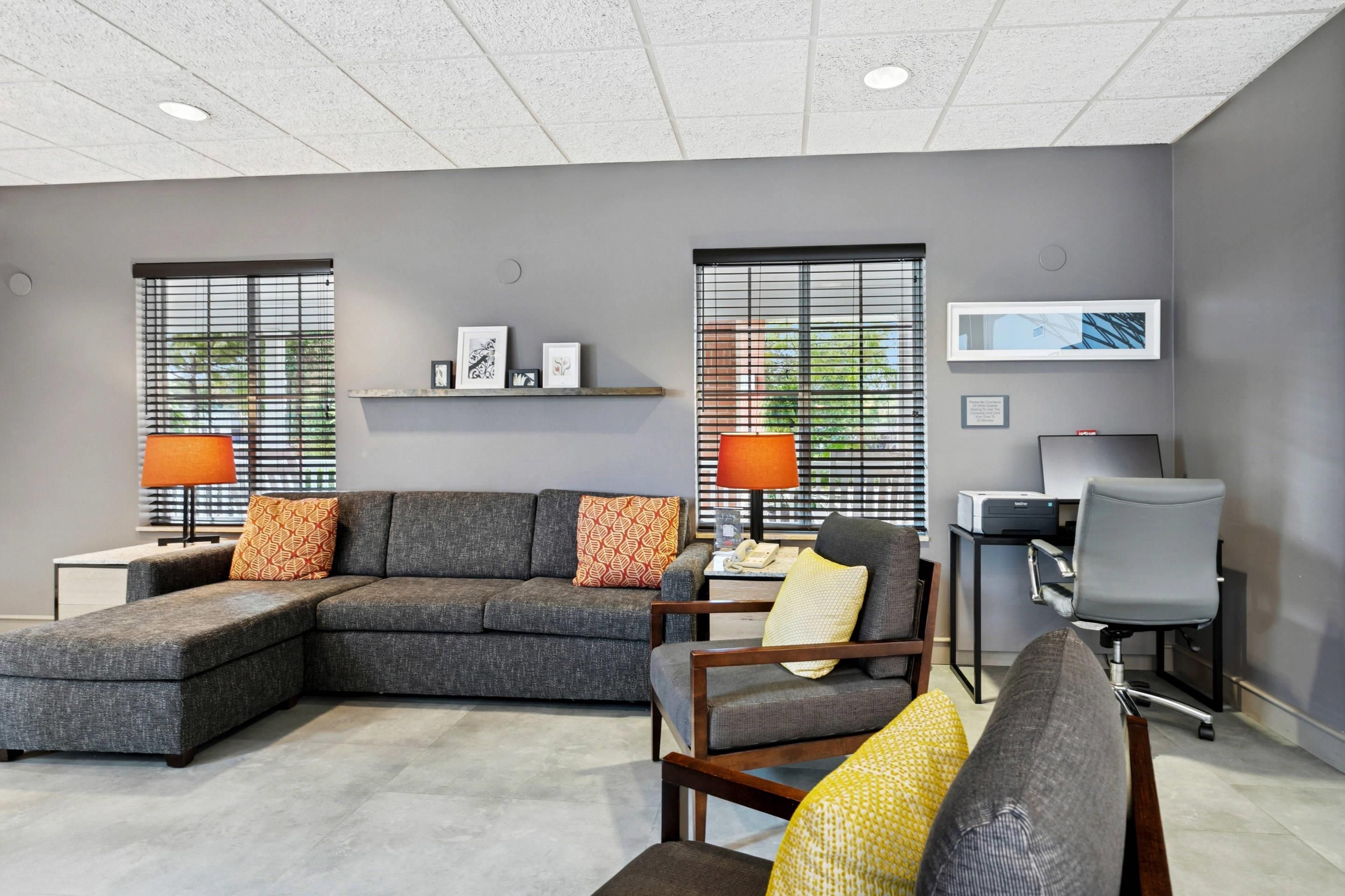 A modern office space with a sectional sofa, two armchairs, a desk with a computer, and a printer.