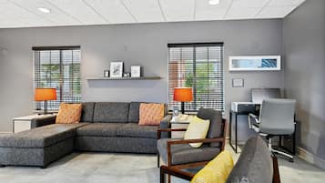 A modern office space with a sectional sofa, two armchairs, a desk with a computer, and a printer.