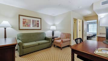 Una habitación de hotel con un sofá verde, un sillón a rayas, un escritorio de madera y una cama con vistas al exterior.