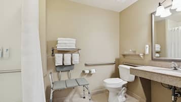 Baño con inodoro, lavamanos, espejo y un banco accesible para silla de ruedas.