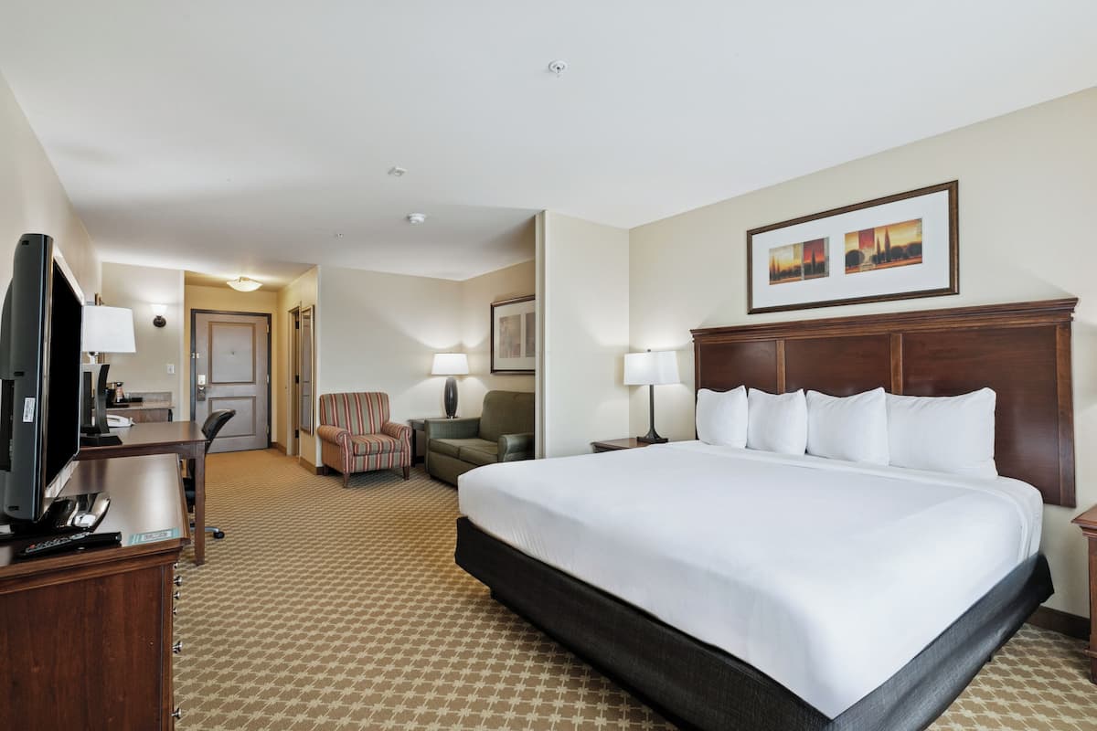 A hotel room with a large bed, a desk with a television, a chair, and a lamp.