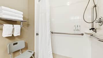 Une salle de bain équipée d’une douche, d’une barre d’appui, d’un porte-serviettes avec des serviettes et d’un petit tabouret.