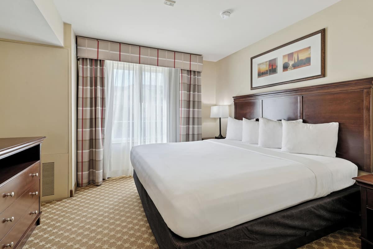A hotel room with a large bed, a dresser, a lamp, and a window with curtains.