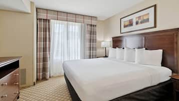 A hotel room with a large bed, a dresser, a lamp, and a window with curtains.