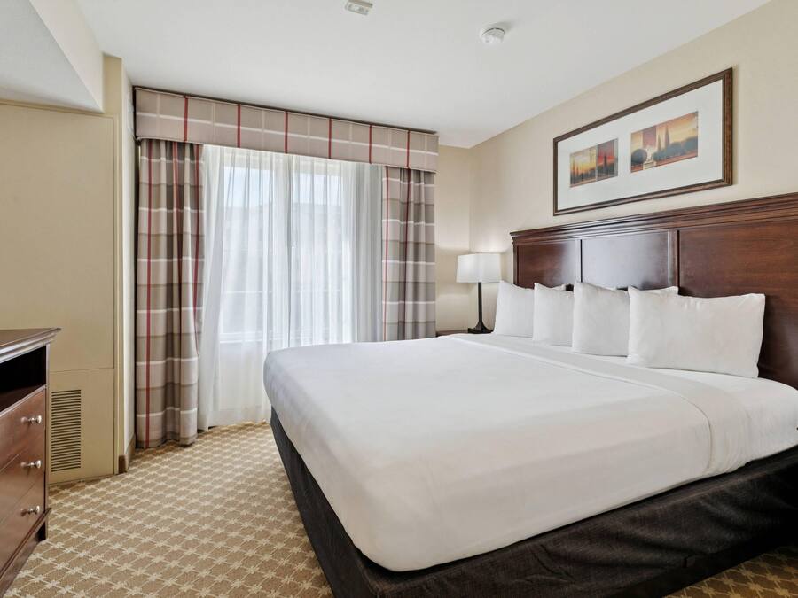 Habitación de hotel con una cama grande, un tocador, una lámpara y una ventana con cortinas.