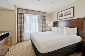 A hotel room with a large bed, a dresser, a lamp, and a window with curtains. - Country Inn & Suites by Radisson, Covington, LA (Covington)