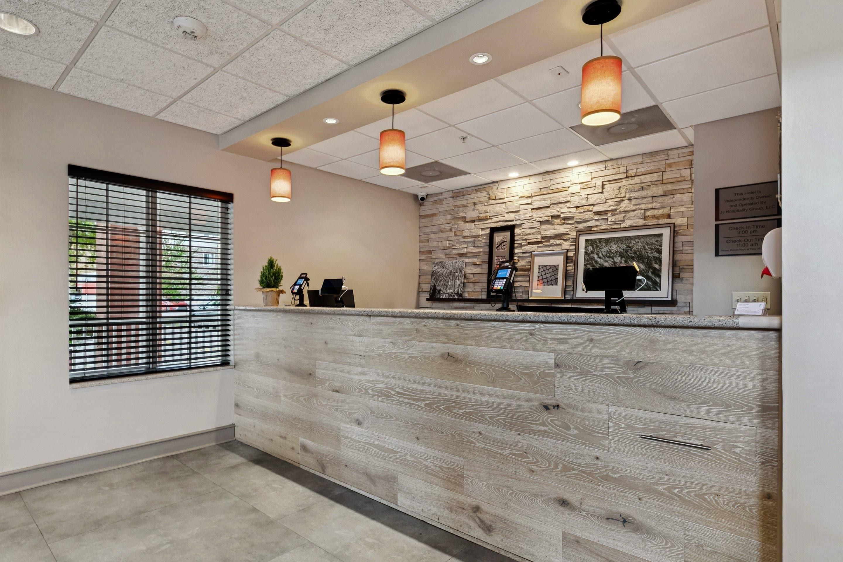 A hotel reception area with a wooden reception desk, a stone wall, and a window with blinds.