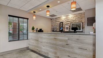 A hotel reception area with a wooden reception desk, a stone wall, and a window with blinds.