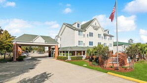 Un hotel con acceso cubierto, un asta de bandera y un césped bien cuidado.