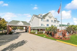 A hotel with a covered entrance, a flagpole, and a well-maintained lawn. - Country Inn & Suites by Radisson, Covington, LA (Covington)