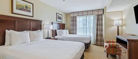 A hotel room with two beds, a desk, a chair, a lamp, and a television.