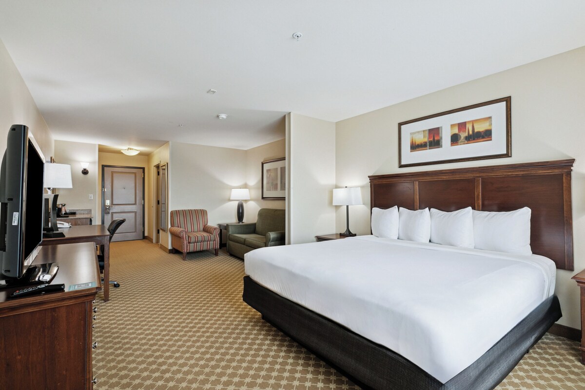 A hotel room with a large bed, a desk with a television, a chair, and a lamp.