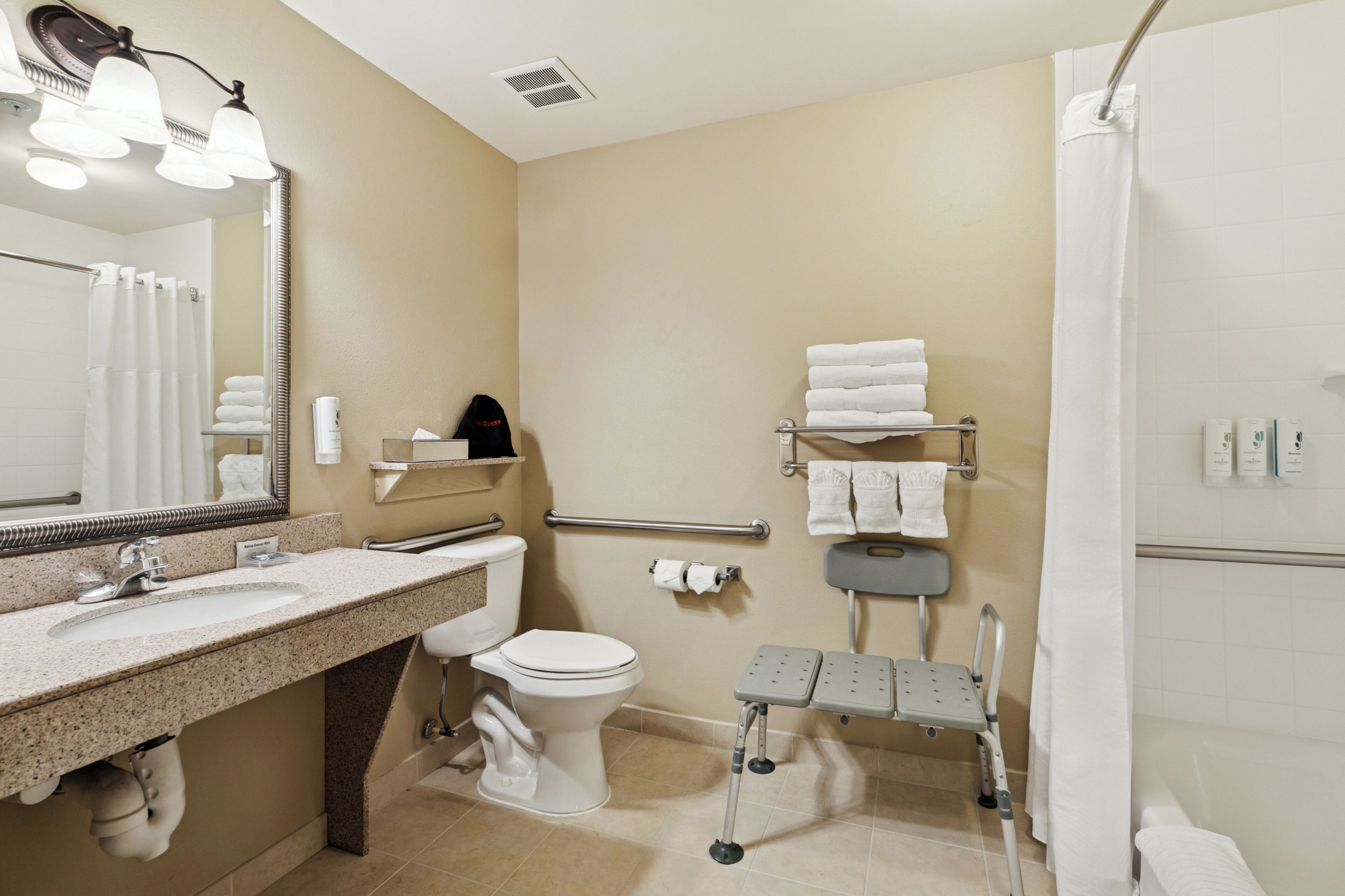 A modern bathroom with a sink, toilet, and shower. It includes a mirror, towel rack, and a grab bar for safety.