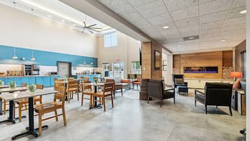A spacious dining area with wooden tables and chairs, a kitchen area with blue cabinets, and a living area with a fireplace and comfortable seating.