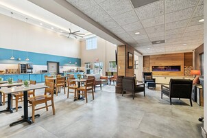 Un comedor amplio con mesas y sillas de madera, una zona de cocina con armarios azules y un salón con chimenea y asientos cómodos.