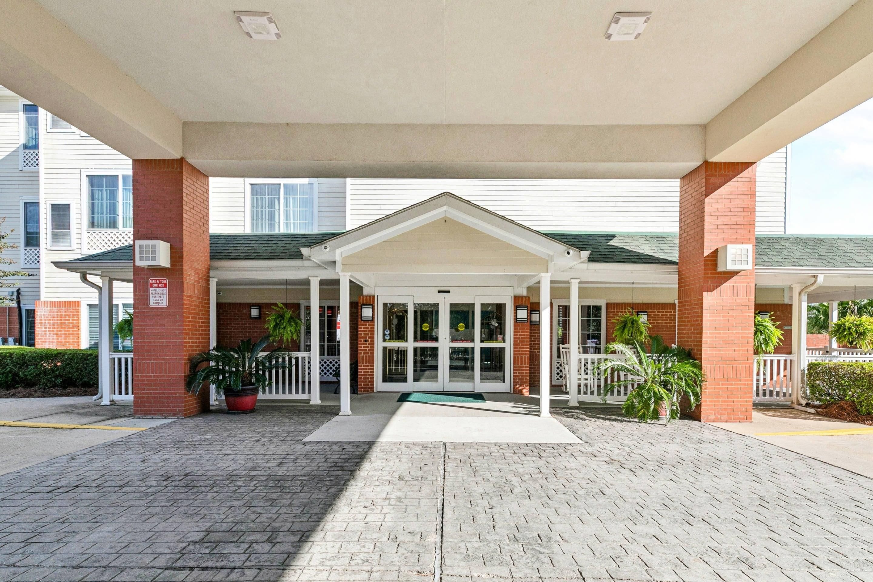 A hotel entrance with a covered walkway, brick pillars, and potted plants.