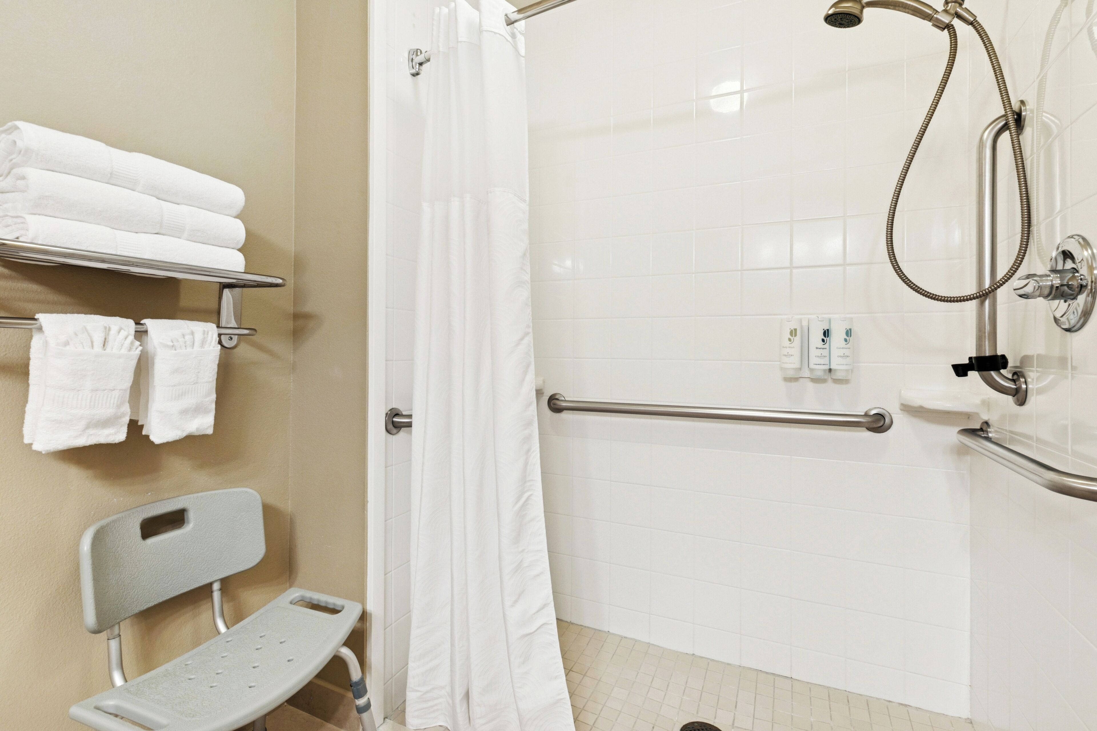 A bathroom with a shower, grab bars, a bench, and a towel rack.