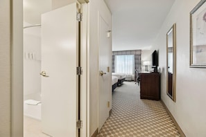 A hotel hallway with a bathroom, a bed, a desk, and a mirror. - Country Inn & Suites by Radisson, Covington, LA (Covington)
