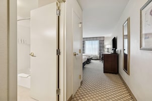 Un pasillo de hotel con un baño, una cama, un escritorio y un espejo.