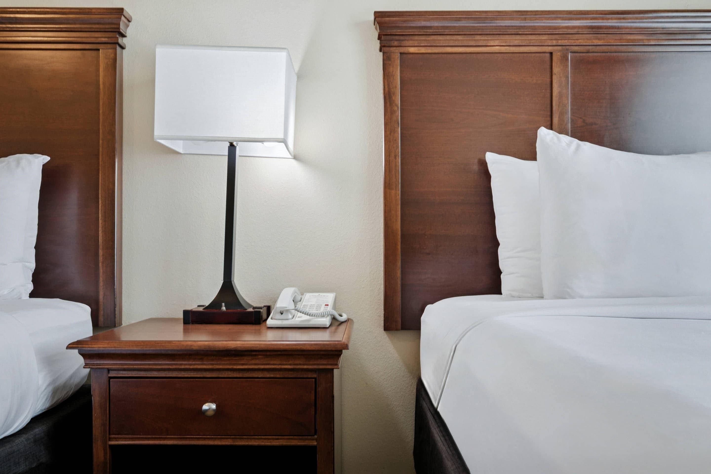 A hotel room with two beds, a nightstand with a lamp, and a telephone.