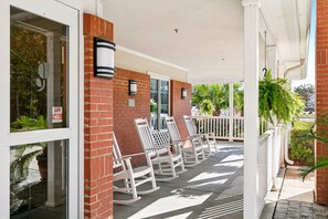 A covered porch with white rocking chairs and a brick wall.