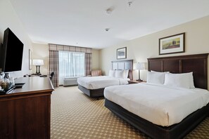 A hotel room with two beds, a desk, a television, and a window with curtains.