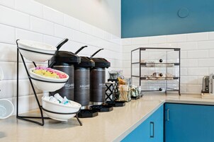 Una zona de cocina con una barra de buffet, que incluye un bol de comida, dispensadores de condimentos y una vitrina de cristal.