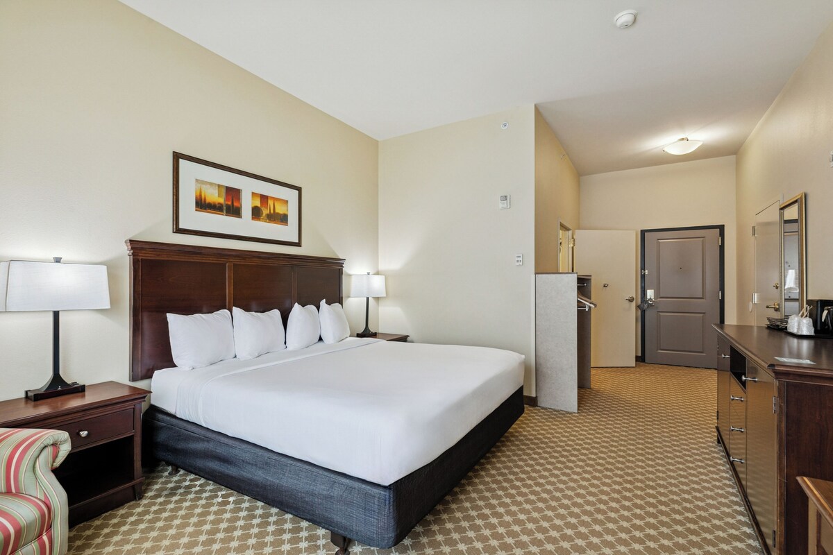 A hotel room with a large bed, bedside lamps, a small desk, a chair, a door, and a mirror.