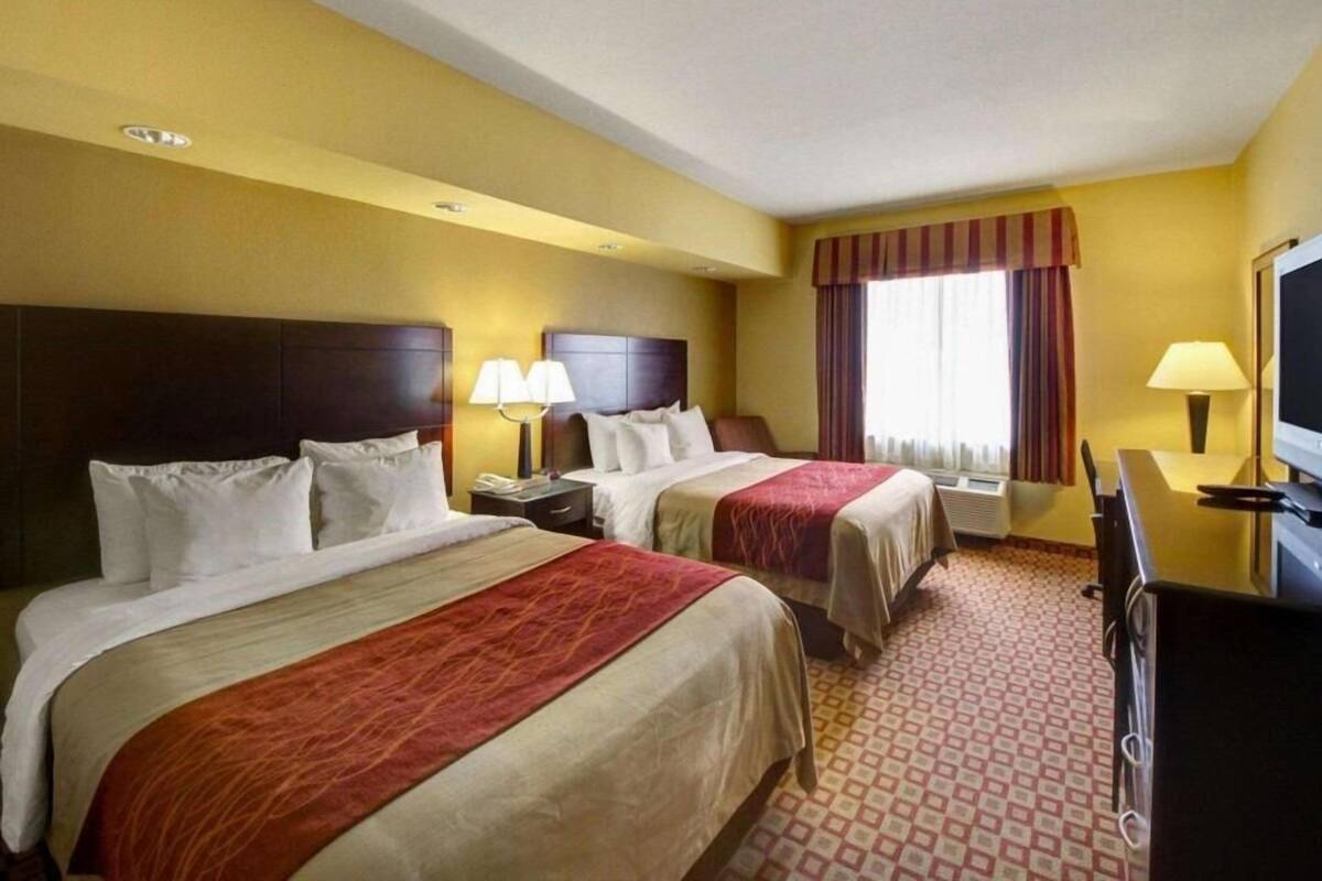 A hotel room with two beds, a television, a desk, and a window with curtains.