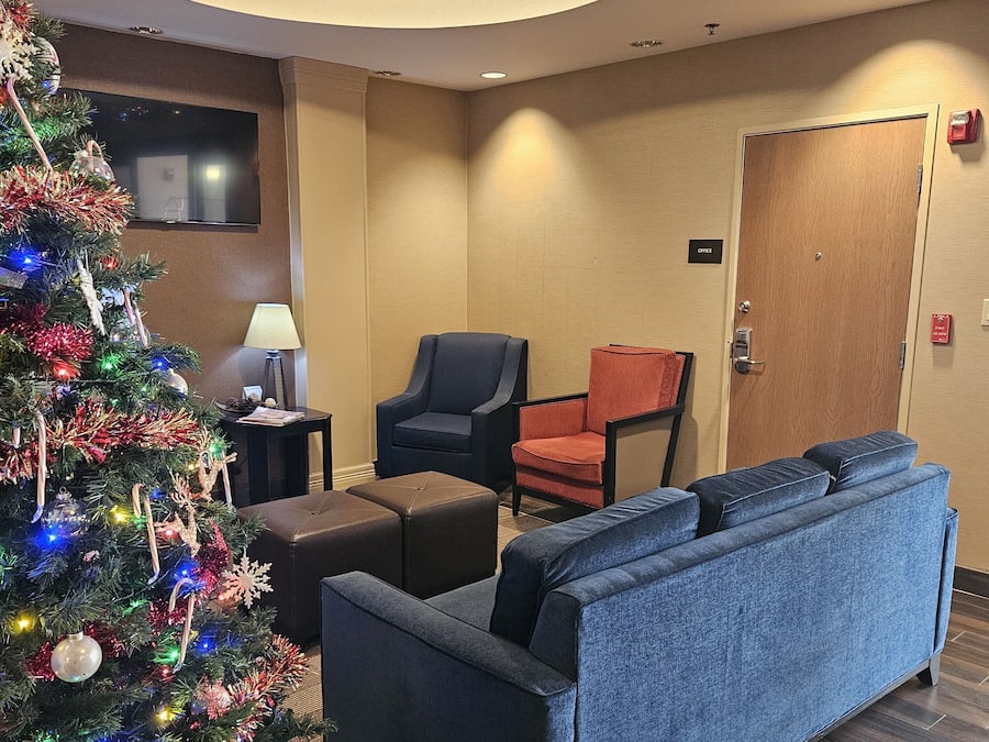 Un vestíbulo de hotel con un árbol de Navidad, un sofá azul, dos sillones, una mesita con una lámpara y una puerta de madera con la etiqueta 'Office'.