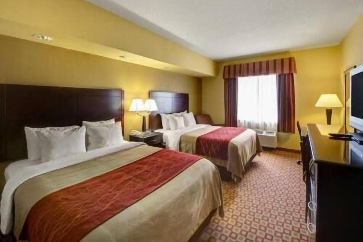 A hotel room with two beds, a television, a desk, and a window with curtains.