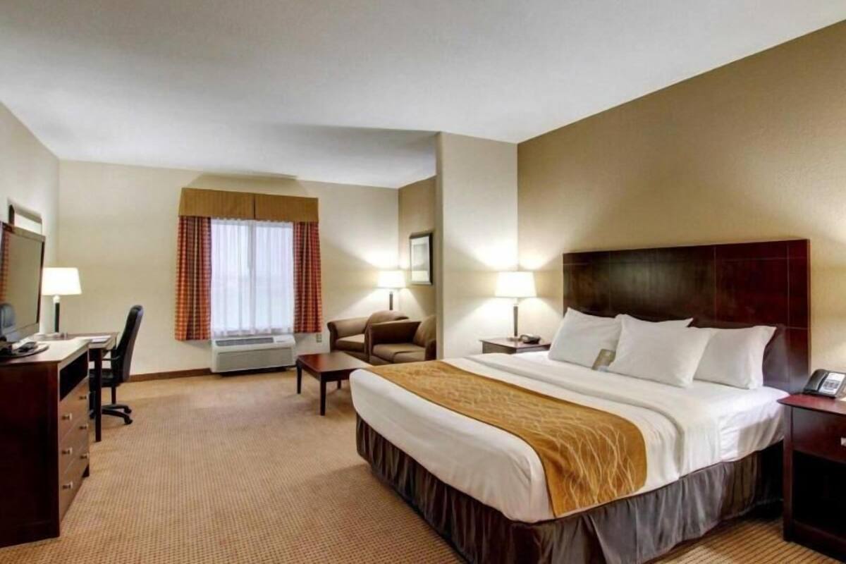 A hotel room with a bed, desk, chair, and a window with curtains.