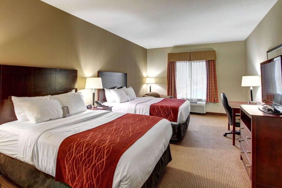 A hotel room with two beds, a desk, a chair, a TV, and a window with curtains.
