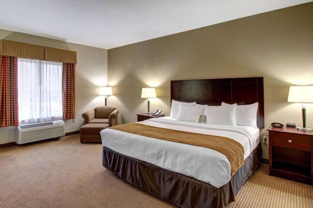 A hotel room with a large bed, two bedside lamps, a chair, a desk, and a window with curtains.