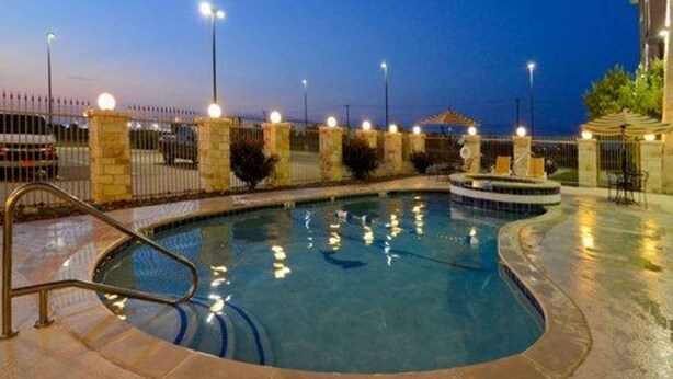 A swimming pool with a stone border and a fountain, surrounded by a fence with lights. - Comfort Inn & Suites Alvarado (Alvarado)