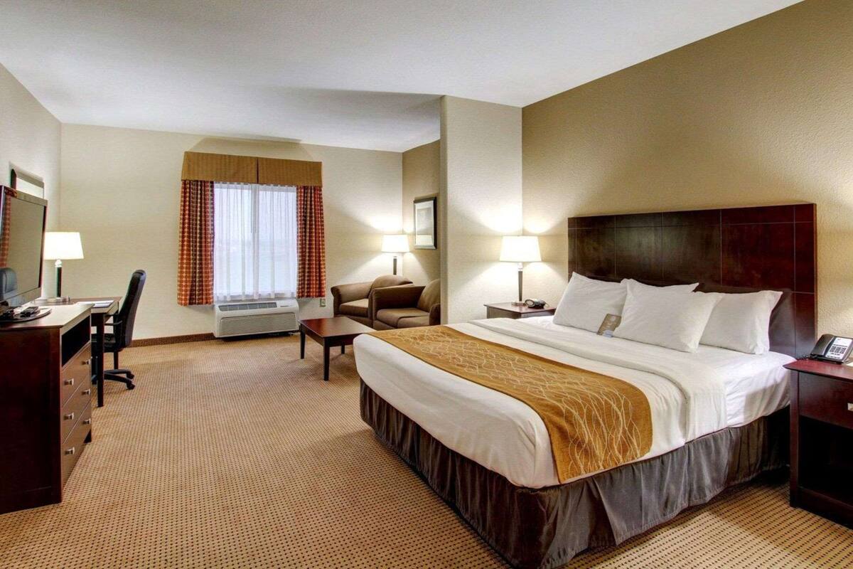 A hotel room with a bed, desk, chair, and a window with curtains.