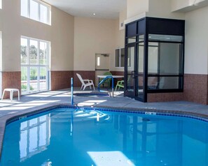 An indoor swimming pool with clear blue water, surrounded by beige walls and a glass enclosure. - Comfort Inn & Suites Harrisonville (Harrisonville)