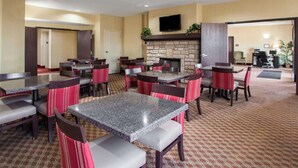Un vestíbulo de hotel con varias mesas y sillas, una chimenea de piedra y un televisor de pantalla plana montado en la pared.