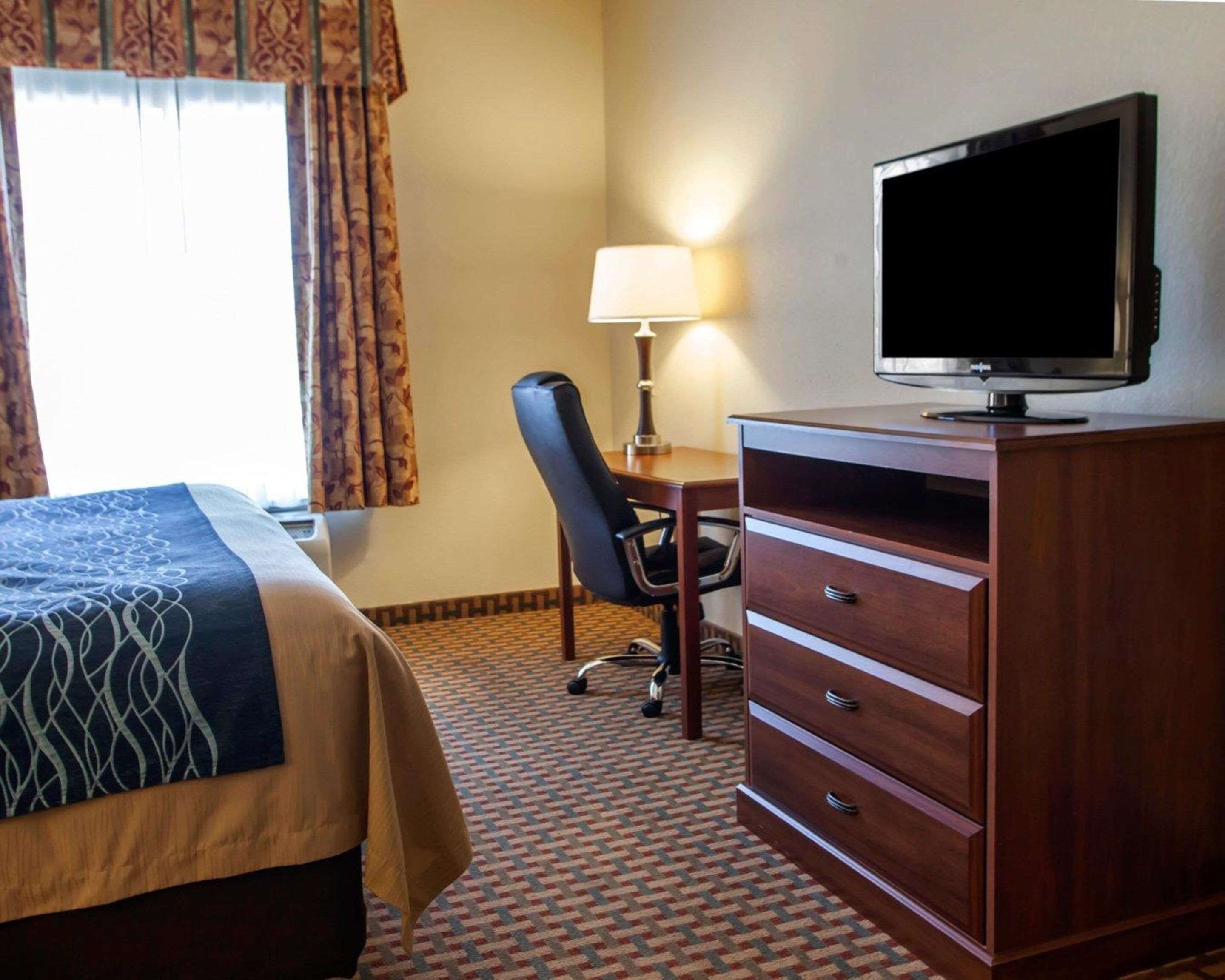 A hotel room with a bed, a desk with a chair, a television, and a dresser.