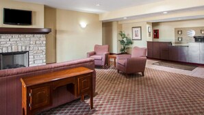 Un vestíbulo de hotel con chimenea de piedra, zona de estar con sofás y sillones, un televisor montado en la pared y un mostrador de recepción.
