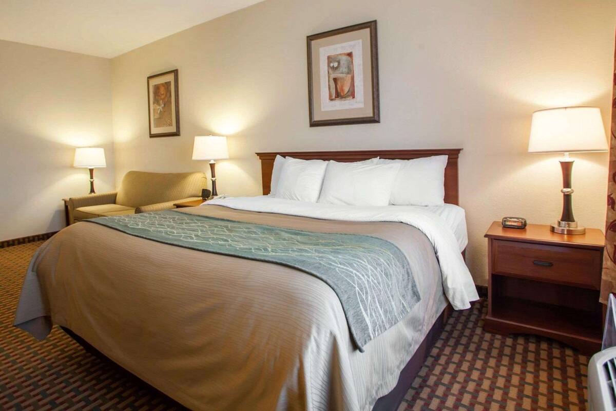A hotel room with a large bed, two bedside tables with lamps, a chair, and two framed pictures on the wall.