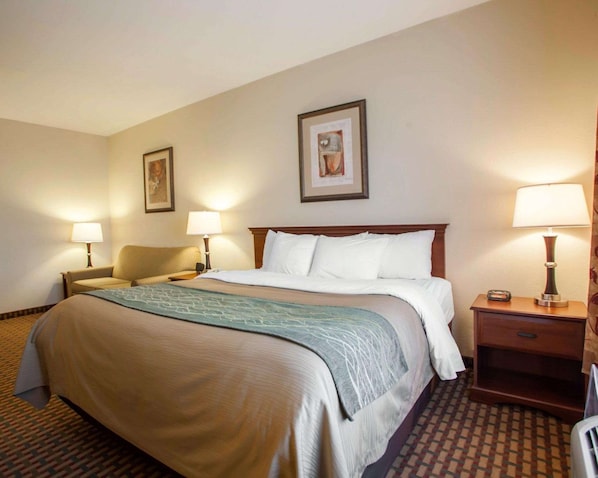 Une chambre d’hôtel avec un grand lit, deux tables de chevet avec des lampes, une chaise et deux tableaux encadrés au mur.