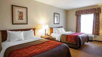A hotel room with two beds, a large window with curtains, and a patterned carpet.