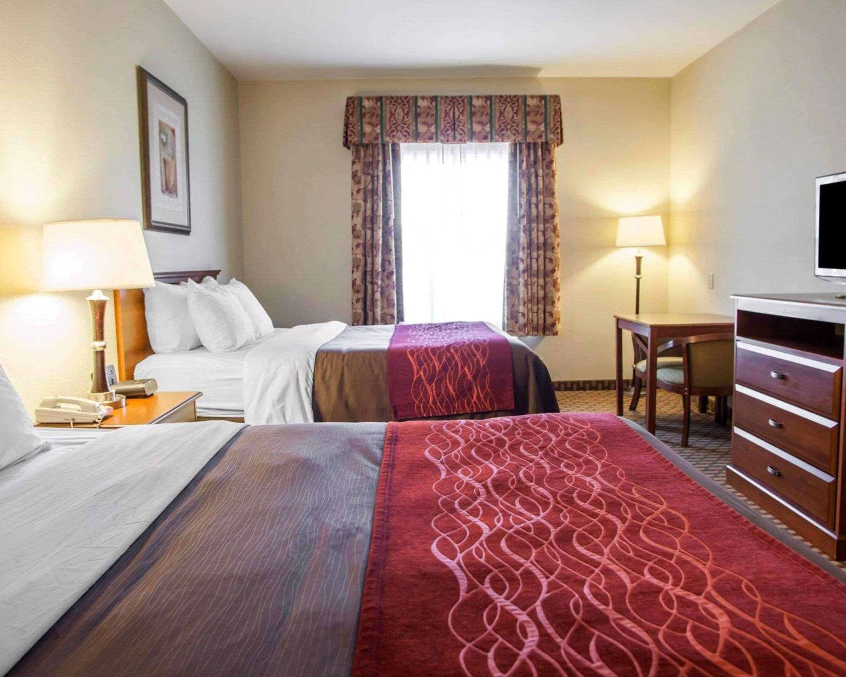 A hotel room with two beds, a desk, a chair, a TV, and a window with curtains.