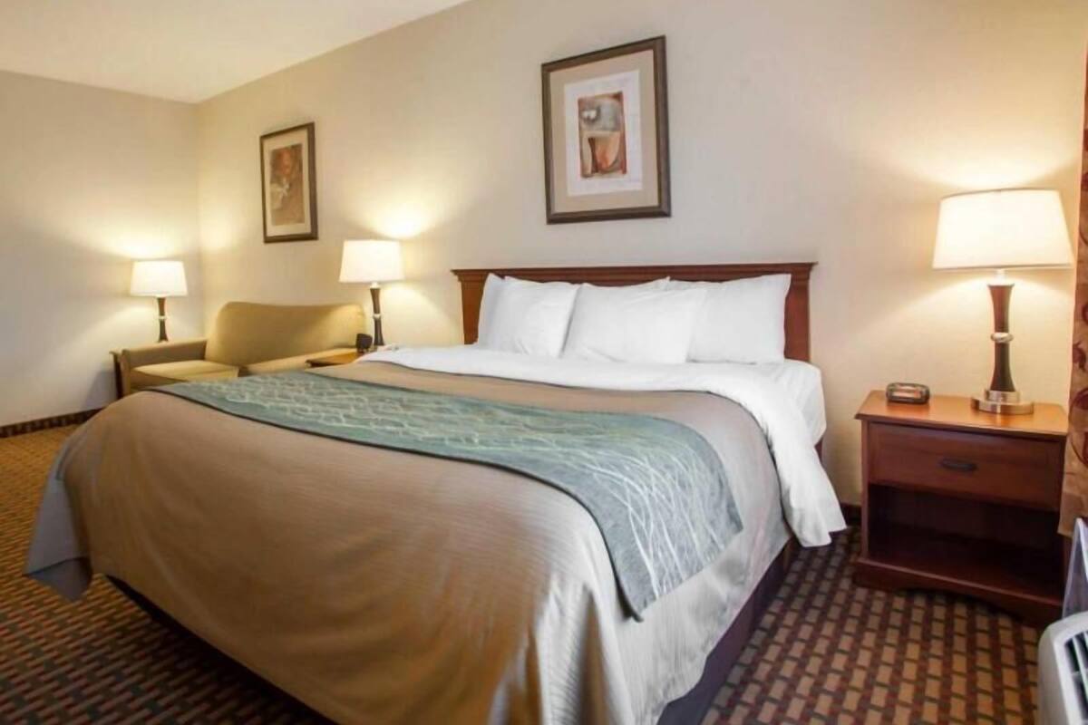 A hotel room with a large bed, two bedside tables with lamps, a chair, and a framed picture on the wall.