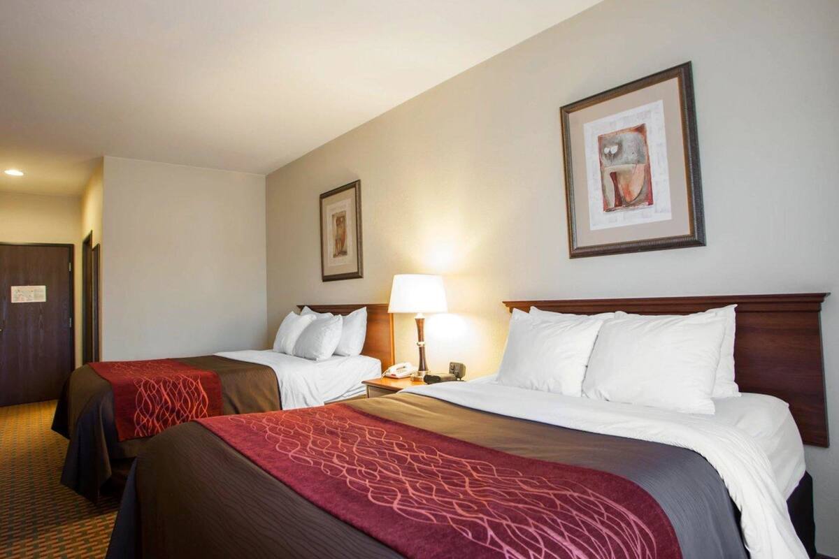 A hotel room with two beds, a nightstand with a lamp, and framed artwork on the walls.